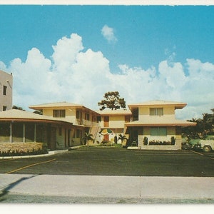 Könnte beinhalten: Eine Vintage-Postkarte zeigt ein zweistöckiges Motel mit gelben Außenwänden, einem Flachdach und einem großen Parkplatz im Vordergrund. Ein hohes Schild steht auf der rechten Seite und ein mehrstöckiges Gebäude ist links unter blauem Himmel zu sehen.