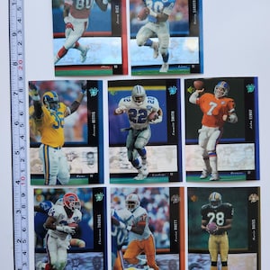 Puede incluir: Una colección de nueve cromos de fútbol con varios jugadores en acción. Las tarjetas tienen un acabado brillante con nombres de jugadores y logotipos de equipos. Los jugadores visten uniformes coloridos y las tarjetas están bordeadas en azul y rojo.