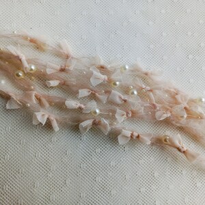 Puede incluir: Delicados hilos decorativos de color rosa p&aacute;lido adornados con peque&ntilde;as perlas de color marfil y diminutos lazos transparentes. Los hilos est&aacute;n hechos de un material suave y esponjoso, creando una est&eacute;tica rom&aacute;ntica y et&eacute;rea. Ideal para manualidades o adornos.