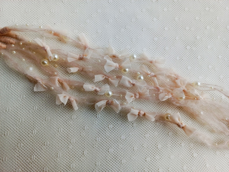 Puede incluir: Delicados hilos decorativos de color rosa p&aacute;lido adornados con peque&ntilde;as perlas de color marfil y diminutos lazos transparentes. Los hilos est&aacute;n hechos de un material suave y esponjoso, creando una est&eacute;tica rom&aacute;ntica y et&eacute;rea. Ideal para manualidades o adornos.