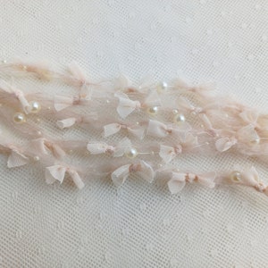 Puede incluir: Delicado adorno decorativo rosa p&aacute;lido con peque&ntilde;os lazos y perlas de imitaci&oacute;n. El adorno est&aacute; hecho de un material transparente y vaporoso. Ideal para embellecer manualidades o a&ntilde;adir elegancia a la ropa.
