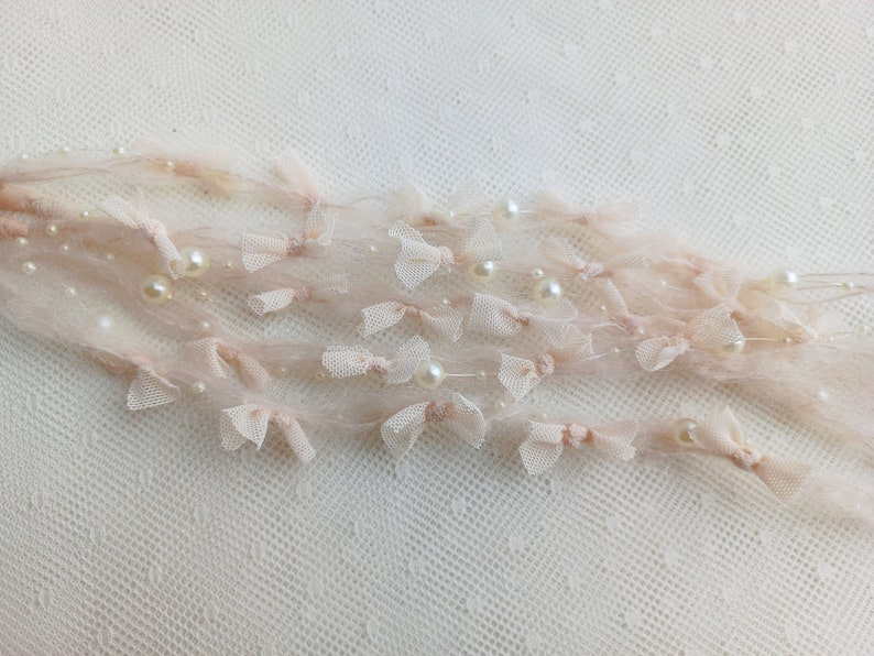 Puede incluir: Delicado adorno decorativo rosa p&aacute;lido con peque&ntilde;os lazos y perlas de imitaci&oacute;n. El adorno est&aacute; hecho de un material transparente y vaporoso. Ideal para embellecer manualidades o a&ntilde;adir elegancia a la ropa.