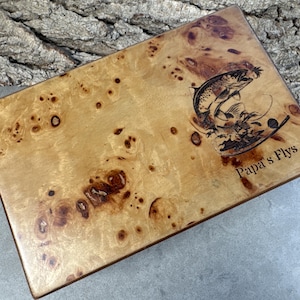 K&ouml;nnte beinhalten: Eine Holzkiste mit einer nat&uuml;rlichen Holzmaserung. Die Kiste hat ein eingebranntes Bild eines springenden Fisches und den Text "Papa's Flys".