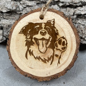 May include: A wooden ornament featuring a laser-engraved image of a Border Collie dog with its paw raised in a friendly gesture. The dog is smiling with its tongue sticking out.