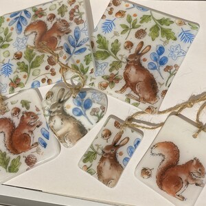 May include: A set of five decorative glass ornaments featuring woodland animals. The ornaments are painted with squirrels, rabbits, and a fox in a whimsical style. The ornaments are perfect for adding a touch of nature to your home decor.