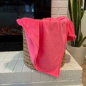 May include: A bright pink fleece blanket folded and placed in a woven wicker basket.
