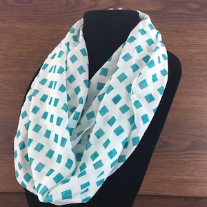 May include: White infinity scarf with a teal diamond pattern.