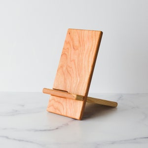 A Cherry Wooden cell phone stand on a white marble counter top.