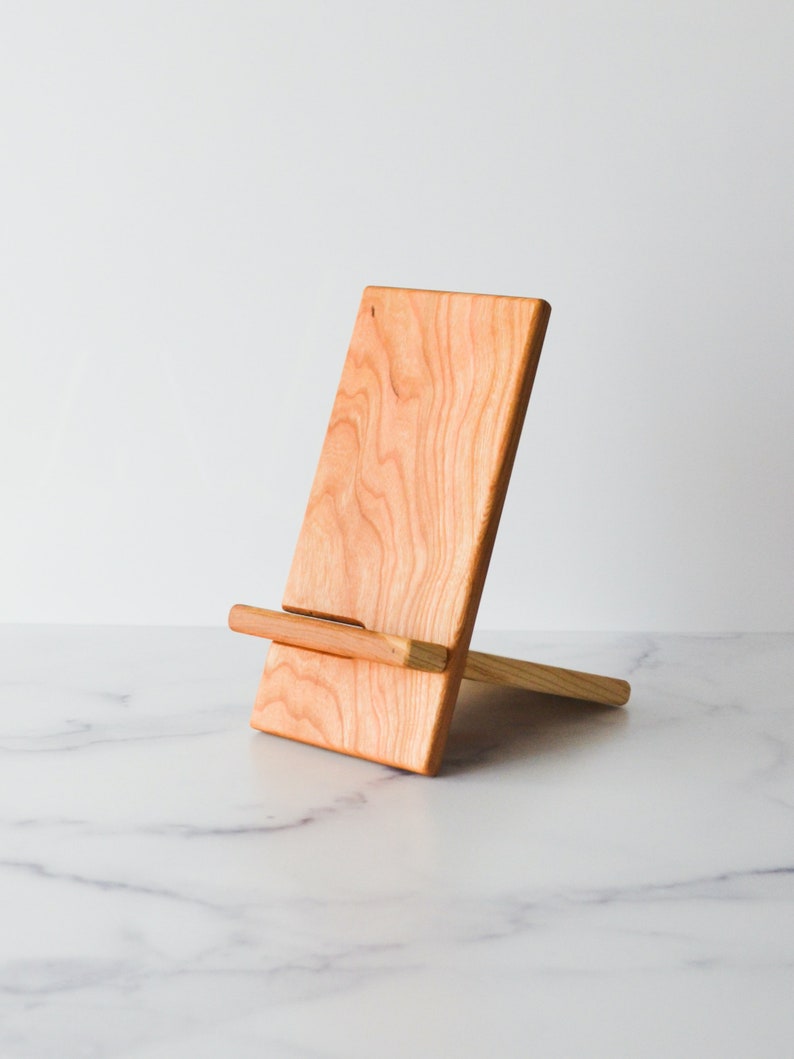 A Cherry Wooden cell phone stand on a white marble counter top.