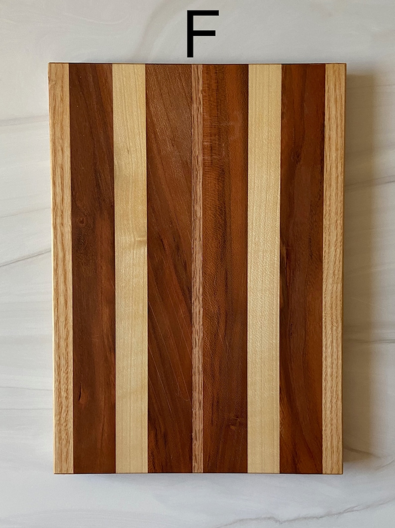 Puede incluir: Una tabla de cortar rectangular de madera con un patr&oacute;n de rayas de madera clara y oscura. La tabla est&aacute; hecha de varios tipos de madera, incluyendo arce y nogal. La tabla est&aacute; etiquetada con la letra "F".