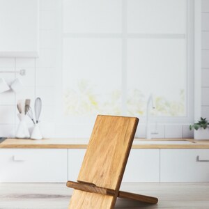 A mid-tone ash wooden cell phone stand on a kitchen counter.