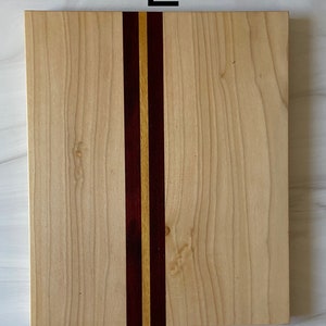Puede incluir: Una tabla de cortar rectangular de madera con una franja vertical de madera de color morado oscuro y amarillo claro.