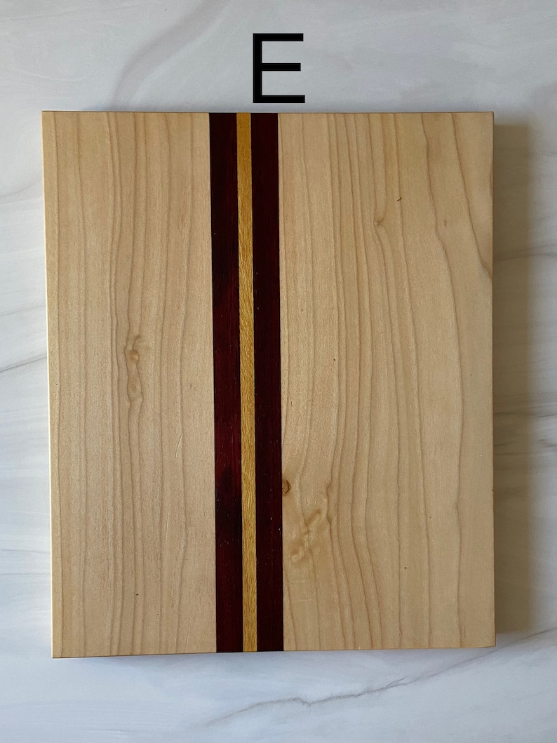 Puede incluir: Una tabla de cortar rectangular de madera con una franja vertical de madera de color morado oscuro y amarillo claro.