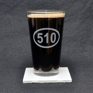 Könnte beinhalten: Ein klares Glas Pint-Glas mit einer dunkelbraunen Flüssigkeit darin. Das Glas hat einen weißen Kreis mit der Nummer "510" darauf gedruckt.
