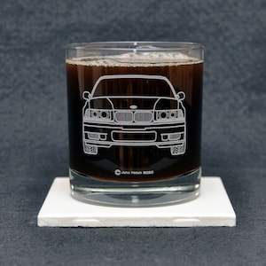 May include: A clear glass tumbler with a dark liquid inside. The glass has a white outline of a car etched into the side. The text "John Hatch 2020" is visible at the bottom of the glass.