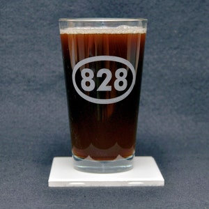 Könnte beinhalten: Ein klares Glas Pint-Glas mit einer dunkelbraunen Flüssigkeit darin. Das Glas hat einen weißen Kreis mit der Nummer "828" eingraviert.