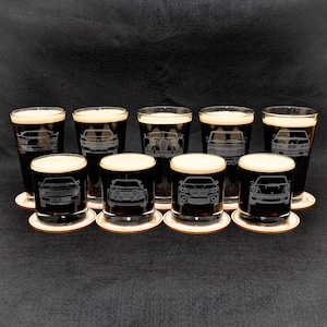 May include: Eight clear glass beer mugs with black liquid inside. Each mug has a different car etched into the glass.