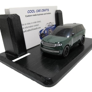 Könnte beinhalten: Ein schwarzer Visitenkartenhalter aus Holz mit einem grünen Miniatur-SUV-Modell. Der Halter hat einen Schlitz für Karten und der Text "COOL CAR CRAFTS" ist auf der Karte zu sehen. Der Halter befindet sich auf weißem Hintergrund.