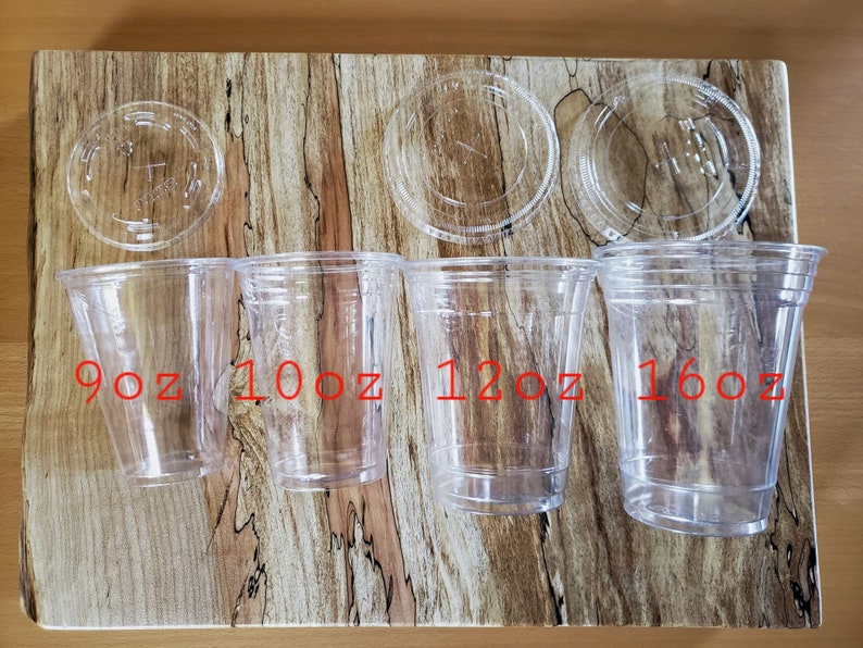 May include: Four clear plastic cups with lids, labeled 9oz, 10oz, 12oz, and 16oz. The cups are arranged in order of size from left to right on a wooden surface.