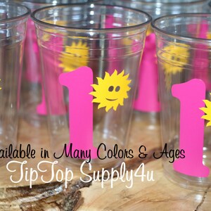 May include: Pink plastic cups with a yellow sun and the number one printed on them. The text "Available in Many Colors & Ages Tip Top Supply4u" is printed on the bottom of the cups.