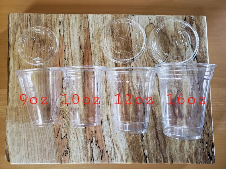 Puede incluir: Cuatro vasos de pl&aacute;stico transparente con tapas, etiquetados 9oz, 10oz, 12oz y 16oz. Los vasos est&aacute;n dispuestos en orden de tama&ntilde;o de izquierda a derecha sobre una superficie de madera.