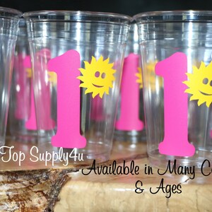 May include: Clear plastic cups with pink number one and yellow sun designs. The text "Tip Top Supply4u" and "Available in Many Colors & Ages" is printed below the cups.