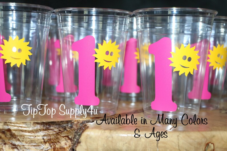 May include: Clear plastic cups with pink number one and yellow sun designs. The text "Tip Top Supply4u" and "Available in Many Colors & Ages" is printed below the cups.