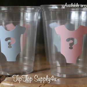 May include: Clear plastic cups with a question mark inside a baby onesie design. The onesies are in pink and blue. The text "Available in Many Colors" is at the top of the image. The text "TipTop Supply4u" is at the bottom of the image.
