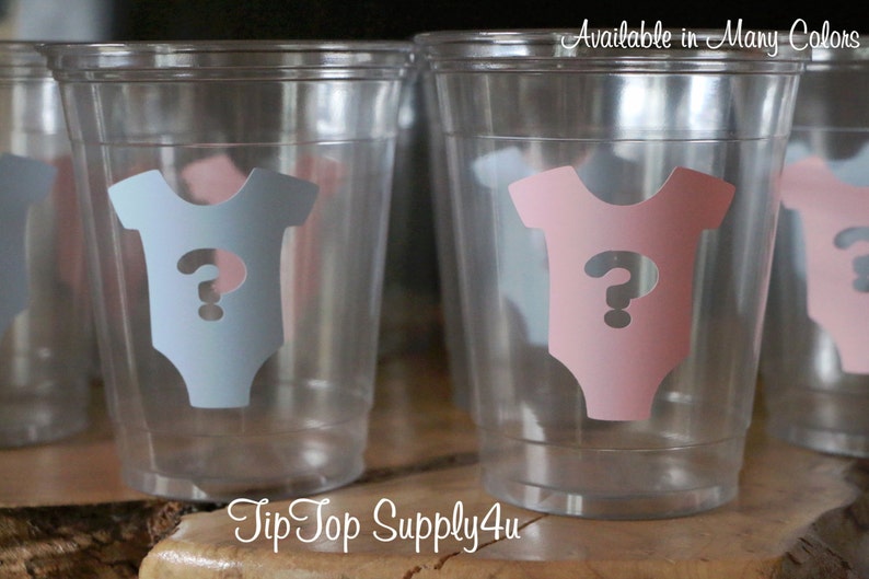 May include: Clear plastic cups with a question mark inside a baby onesie design. The onesies are in pink and blue. The text "Available in Many Colors" is at the top of the image. The text "TipTop Supply4u" is at the bottom of the image.