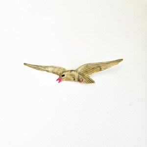 Può includere: Un broche vintage a forma di uccello in legno intagliato con un becco rosa e un occhio di strass rosa. L'uccello è in volo con le ali spiegate.
