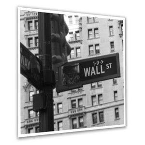 May include: A black and white photograph of a street sign that reads "1-9-> Wall St". The sign is mounted on a pole with a traffic light above it. The sign is in front of a tall building with many windows.