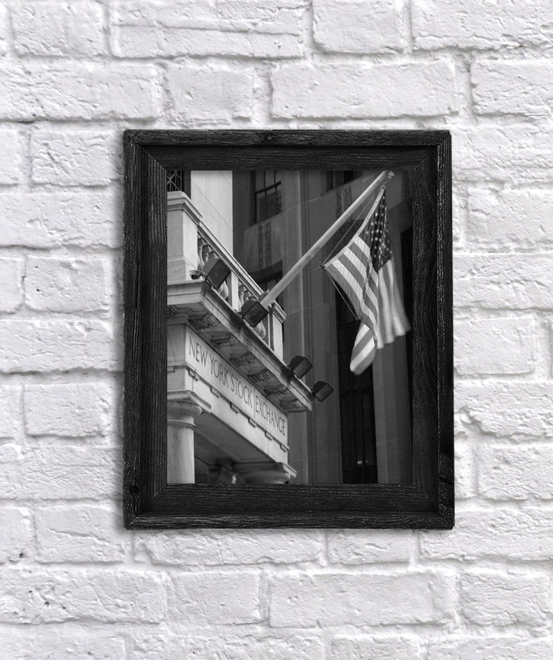 May include: Black and white photograph of the New York Stock Exchange building with an American flag waving in the wind.