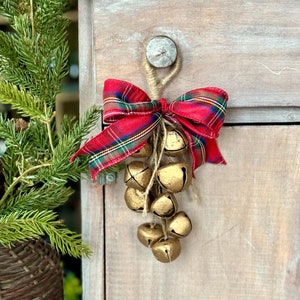 May include: A cluster of gold bells tied with a red and black plaid ribbon and twine, hanging from a wooden cabinet door.