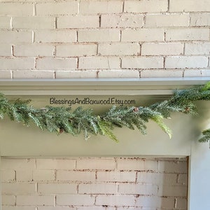 Peut inclure: Une guirlande de pin verte avec des baies rouges drap&eacute; sur une chemin&eacute;e peinte en blanc. La guirlande est d&eacute;cor&eacute;e d'aiguilles de pin givr&eacute;es et de petites pommes de pin. Le texte "BlessingsAndBoxwood.Etsy.com" est visible sur la chemin&eacute;e.