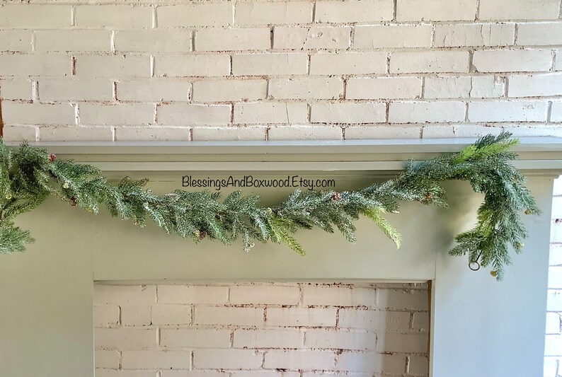 Peut inclure: Une guirlande de pin verte avec des baies rouges drap&eacute; sur une chemin&eacute;e peinte en blanc. La guirlande est d&eacute;cor&eacute;e d'aiguilles de pin givr&eacute;es et de petites pommes de pin. Le texte "BlessingsAndBoxwood.Etsy.com" est visible sur la chemin&eacute;e.