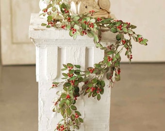 May include: A long garland of artificial greenery with red berries. The garland is draped over a white pedestal.