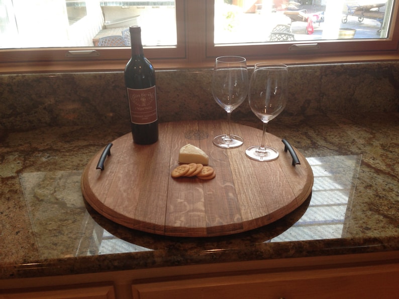 May include: A wooden serving tray with two wine glasses and a bottle of wine. The tray is made from a repurposed wine barrel and has a natural wood finish. There is a small piece of cheese and crackers on the tray.