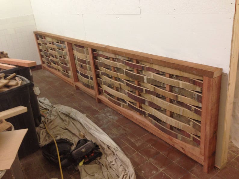 May include: A wall panel made of woven wood slats in shades of brown, beige, and red. The slats are arranged in a wavy pattern and are framed with a natural wood border.
