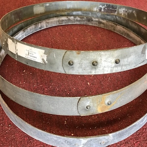 May include: Three metal hoops, likely for a barrel or similar container, stacked on top of each other. The hoops are silver in color and have a slightly rusted appearance. The hoops are labeled with the text "ITEM # GA-MPR1001  Roundhead Hoop".