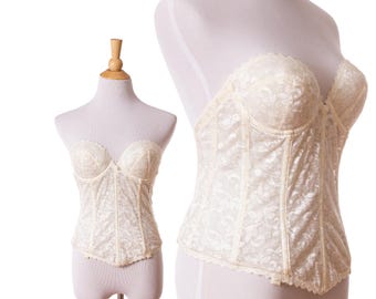 Op de afbeelding: Ivoor kleurig korset met een bloemen kanten patroon, getoond op een mannequin. De strapless bodice heeft een geschulpte rand en gestructureerde baleinen. Het korset is een vintage stijl, die een romantische en elegante esthetiek biedt.