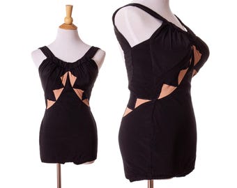 Op de afbeelding: Zwart badpak met beige geometrische uitsparingen. Het badpak heeft een ronde halslijn en dunne bandjes. Het wordt gepresenteerd op een mannequin tegen een witte achtergrond. Vintage stijl.