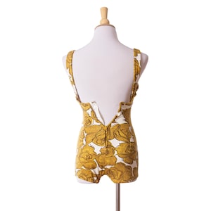 Op de afbeelding: Vintage badpak uit &eacute;&eacute;n stuk met een bloemenrozenpatroon in mosterdgeel en wit. Het badpak heeft een lage rug en een ritssluiting. Het kledingstuk wordt op een mannequin getoond.