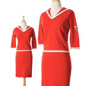 May include: A vintage red knit dress and top set. The top has a V-neck collar and three-quarter sleeves with white trim. The dress has a matching white trim at the waist. The top features an embroidered design on the sleeve.