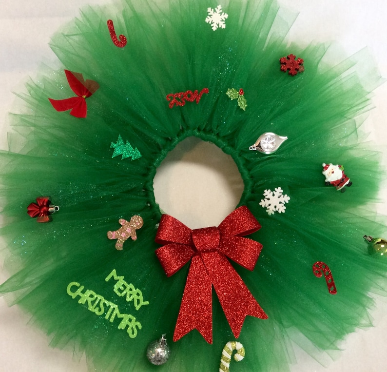 May include: A green tulle Christmas wreath with a red bow, glitter, and various Christmas decorations, including a candy cane, a gingerbread man, a snowflake, a Christmas tree, and the words "Merry Christmas".