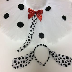 May include: A Dalmatian-themed costume set featuring a white tutu with black spots, a matching tail with a red bow, and a headband with attached ears. The costume is designed for a child and is perfect for a themed party or Halloween.