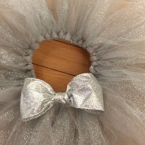 May include: A silver glitter tulle tutu skirt with a matching bow. The skirt is made of layers of shimmering fabric, perfect for dance or dress-up. The bow is centered on the front of the skirt.
