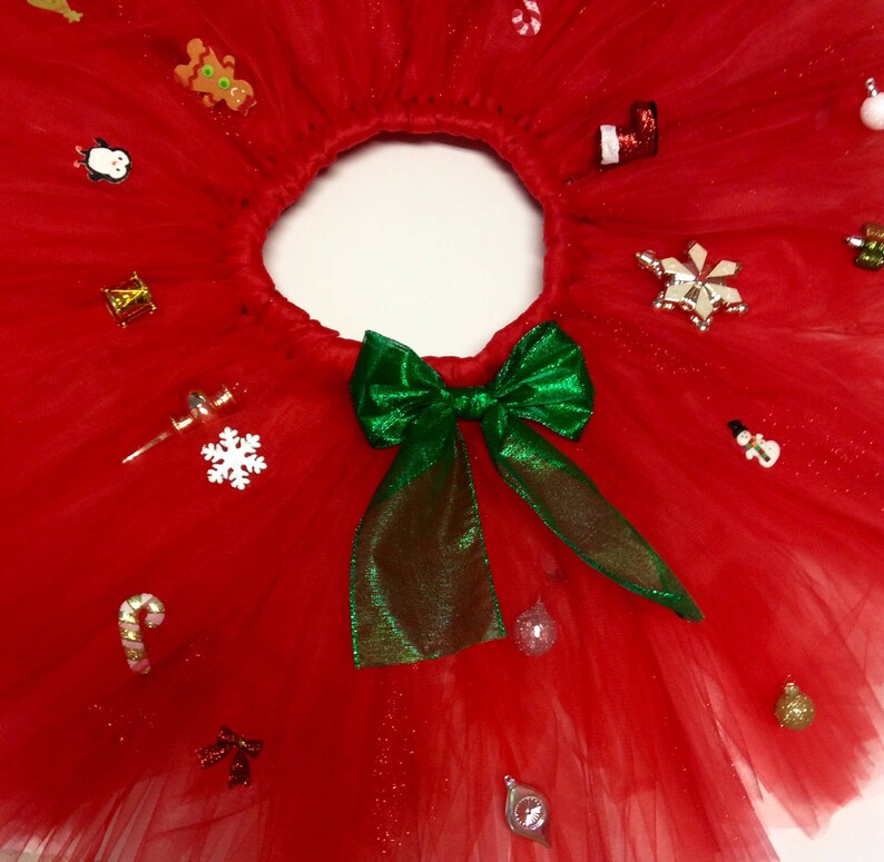 May include: Red tulle tutu skirt with a green bow and various Christmas-themed embellishments, including a snowman, candy cane, and ornaments.