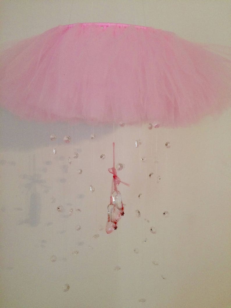 Peut inclure: Un mobile en tulle rose avec un ruban rose et des d&eacute;corations en cristal.