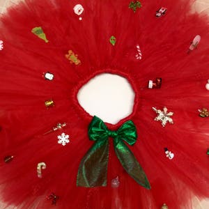 May include: A red tulle tutu skirt with a green bow and various Christmas-themed embellishments, including snowflakes, candy canes, and ornaments.