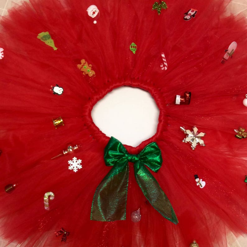 May include: A red tulle tutu skirt with a green bow and various Christmas-themed embellishments, including snowflakes, candy canes, and ornaments.